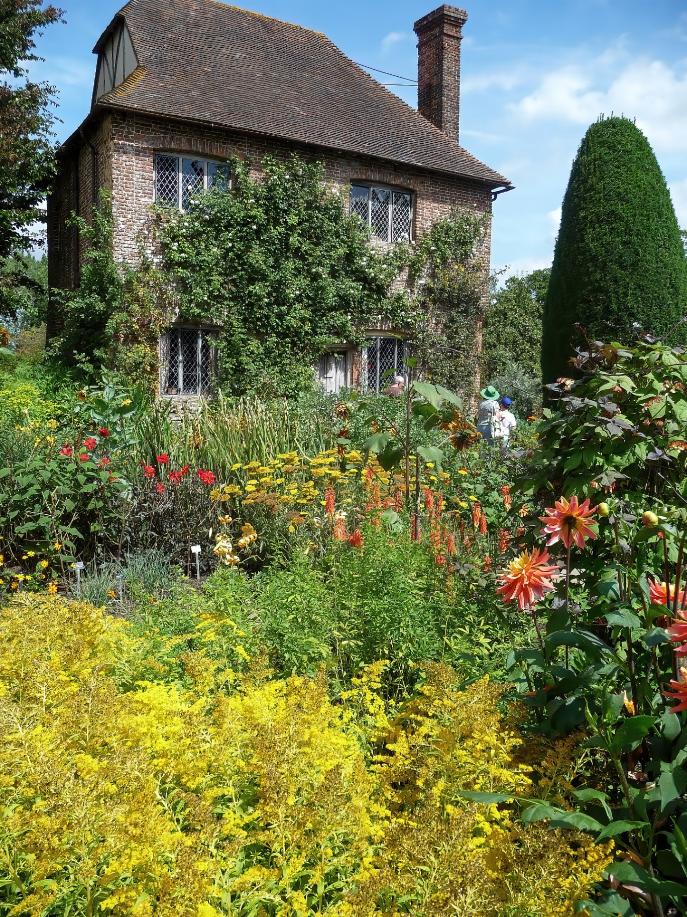 A vertical shot of a garden with colorful flowers and a brick building